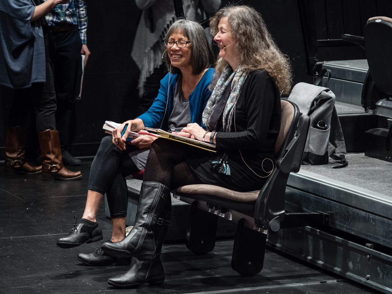 Two women sitting side by side in the front row of an auditorium, laughing nervously.